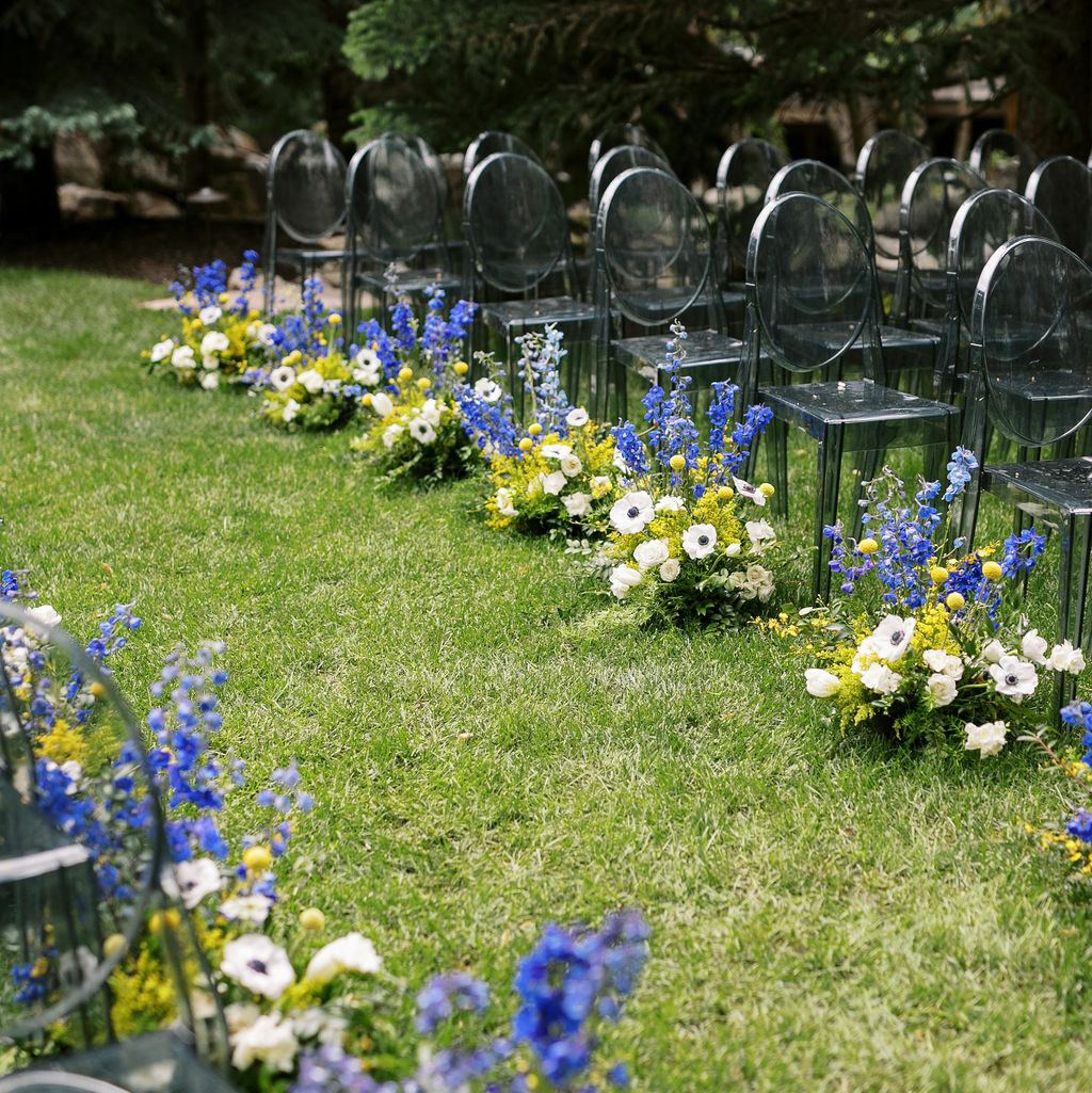Outdoor wedding walkway. Chairs decorated in amazing blue, white and yellow flowers. Wedding scene to remember created by Kaushay & Co Events. #Kaushay&Co #Kaushay&CoWeddings #Wedding #MoodySoiree #UtahWeddings #weddingplannerutah #NorthernUtahEventPlanner